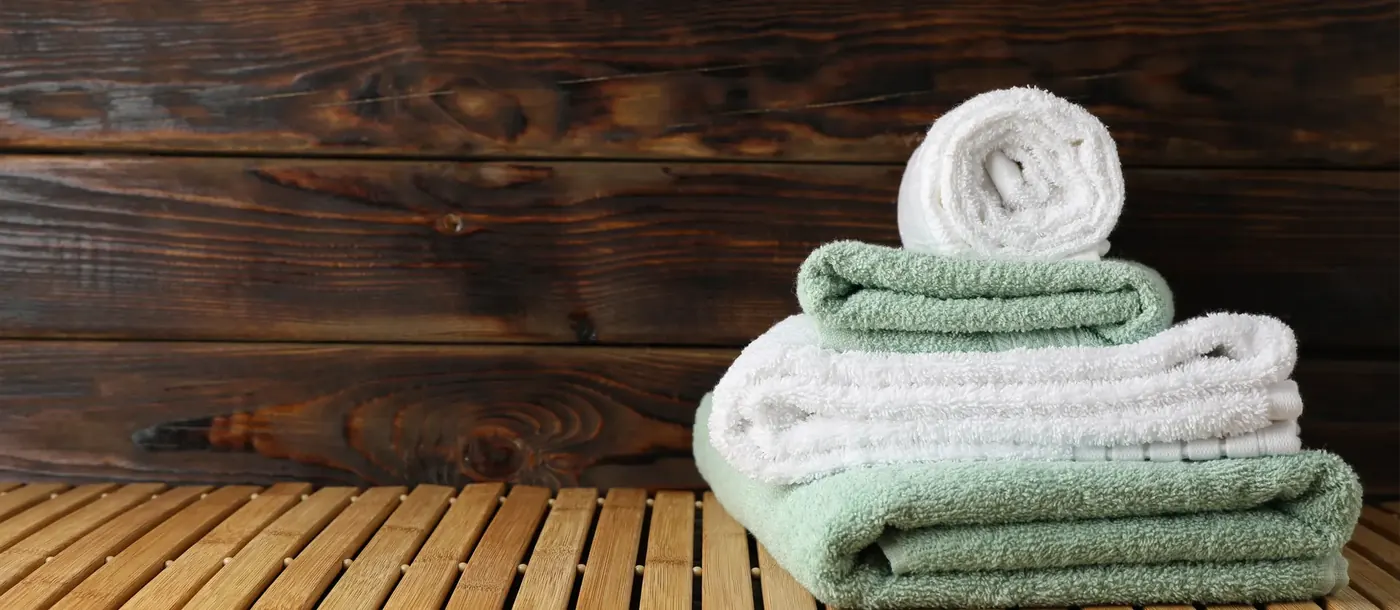 Folded white and sage-green terry towels with a rolled white towel on a slatted wooden bench